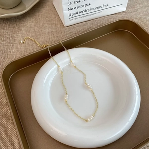 Détail d'un collier en perles d'eau douce sur une assiette en céramique et plateau doré