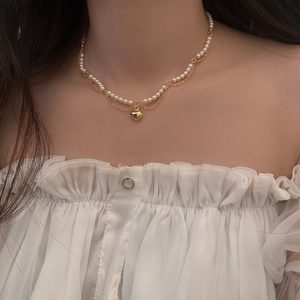 Detail of pearl chain necklace featuring a gold heart pendant on a model's neck