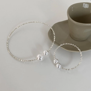 Detail of silver metallic choker and bracelet set with large white pearls on a grey surface