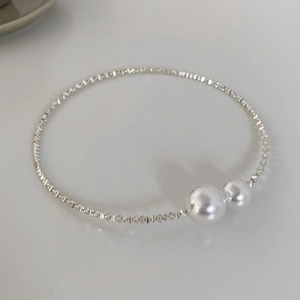 Macro detail of silver beaded choker with white pearls on a minimalist white background