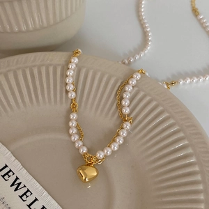 Detail of elegant gold heart pendant with layered pearl necklace on ceramic tray