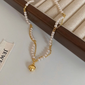 Detail of elegant gold-plated heart pendant and white pearl necklace on wooden display