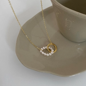 Detail of elegant gold double-loop necklace with pearls resting on a ceramic cup
