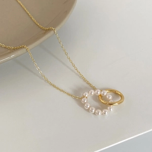 Detailed view of intertwined gold rings with white pearls on a minimalist necklace