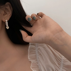 Detail of natural shell heart pearl earrings worn by a model in a close-up elegant view
