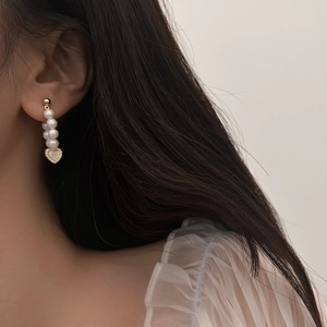 Elegant gold heart earrings with natural shell pendant and white pearls on a model