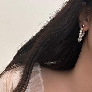Detail view of heart charm drop earrings with white shell pearls worn by a model