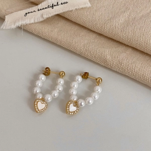 Detailed close-up of heart pearl earrings with white shell inlay and gold plating