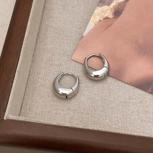 Macro detail of silver drop hoop earrings on a minimalist beige canvas display tray