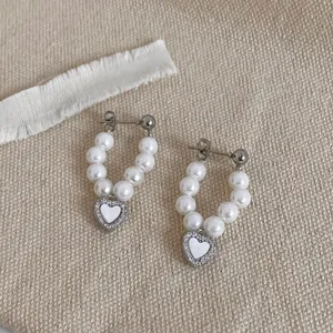 Detailed close-up of heart-shaped pearl earrings with pavé crystals on beige linen