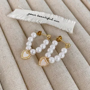 Macro shot of U-shaped gold earrings with white pearls and micro-pave heart shell charm
