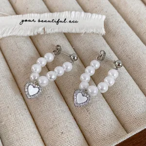 Close-up of pearl heart hoop earrings with micro-inlaid zircon charms on a beige tray