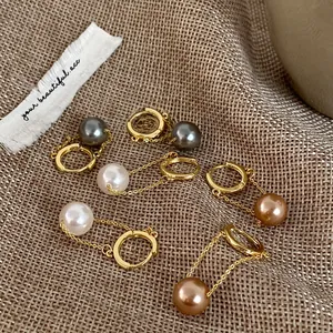 Detail of gold-plated pearl drop earrings in grey, white and champagne colors