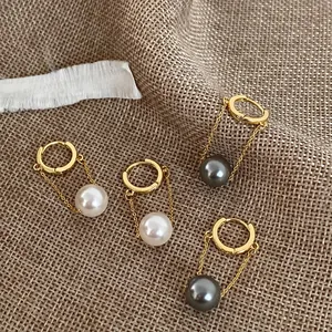 Detail view of pearl drop earrings with long gold chains and hoops on a linen background