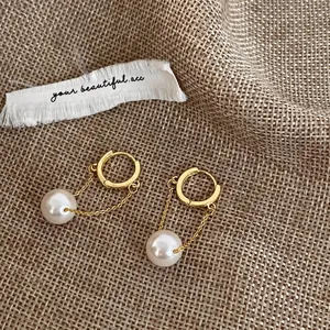 Macro shot of gold hoop earrings with white pearl pendants on woven fabric background