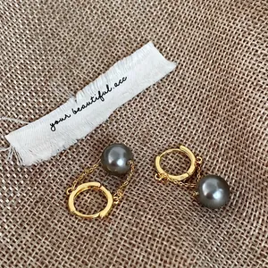 Elegant gold hoop earrings with hanging grey pearl drops on a rustic woven background