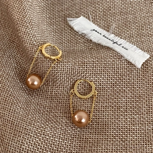 Detail of elegant gold earrings with long chain tassels and shiny brown pearls