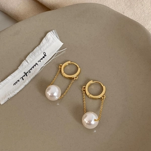 Detail of gold-plated pearl drop earrings with slender chains on a ceramic tray