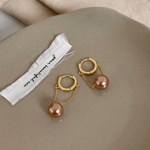 Close-up of gold-plated tassel earrings with pearl pendant in a minimalist tray