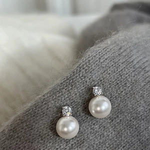 Close-up of pearl stud earrings with zircon inlay on grey knitted fabric background