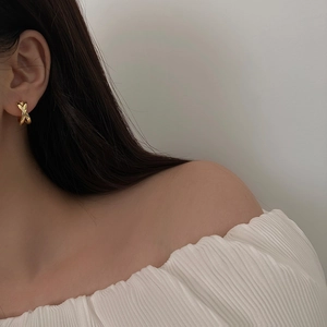 Detail of twisted cross golden metal earrings worn by a model in a minimalist style