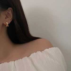 Elegant gold-tone criss-cross hoop earrings worn by a model in a minimalist setting