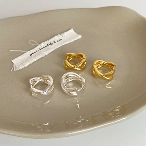 Minimalist twisted hoop earrings in gold and silver finish on a ceramic plate