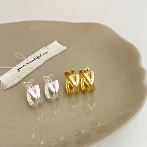 Detail of twisted gold and silver geometric hoop earrings on a ceramic tray