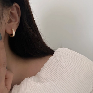 Gros plan d'une boucle d'oreille créole dorée avec zircons brillants portée sur l'oreille