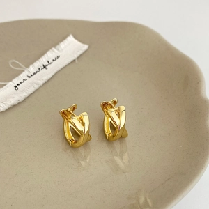 Detail of high-polished gold-plated interlocking cross hoop earrings on a ceramic tray