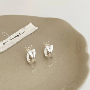 Macro detail of silver intertwined V-shaped geometric earrings on a ceramic tray