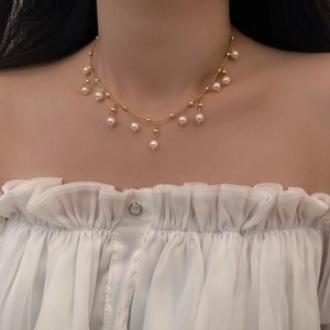Detailed close-up of a gold-plated tassel necklace with elegant white pearls on a model
