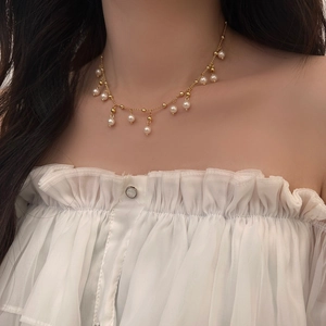 Detail of a gold tassel necklace with white pearls worn on a female collarbone