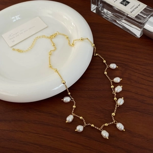 Detail of gold necklace with white teardrop pearls on white ceramic plate