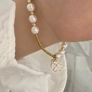 Elegant pearl and gold bracelet featuring a sparkling zircon flower pendant on a wrist