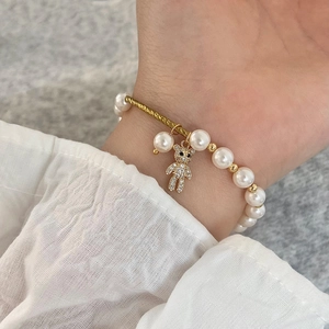Detail of a pearl bracelet with gold hardware and a pavé teddy bear pendant on model