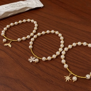 Detail of pearl bracelets with gold fish tail, flower and star pendants on wood