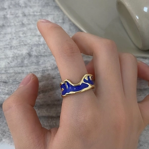 Detail showing wavy gold enamel ring worn on finger against minimalist home decor