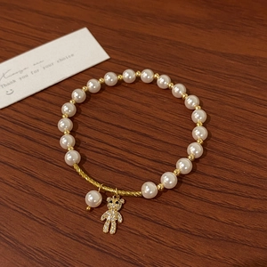 Detail of pearl bracelet with golden bear charm and zircon pendant on wooden surface