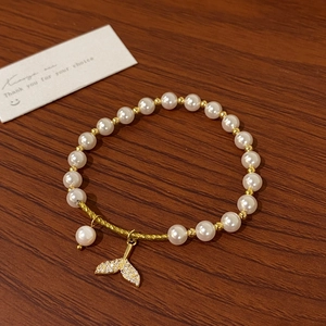 Detail of pearl bracelet with golden mermaid tail pendant and sparkling crystal accents