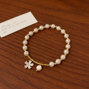 Close-up of pearl bracelet with gold hardware and rhinestone flower pendant on wood
