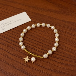 Detail of pearl bracelet with gold spiral bar and sparkling starburst pendant on wood