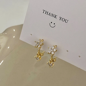 Nahaufnahme goldener Blumenohrringe mit Zirkonia auf einer weißen Displaykarte