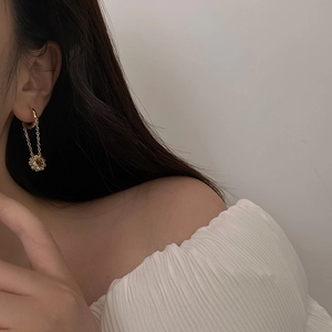 Close-up of gold chain earrings with zircon sunburst pendants worn by a female model