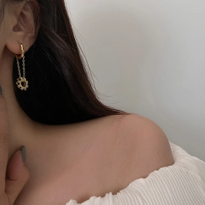 Close-up of elegant gold tassel earrings with gear charm worn by a model