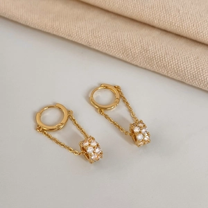 Close-up of gold tassel earrings with zircon cylinder pendants on beige fabric