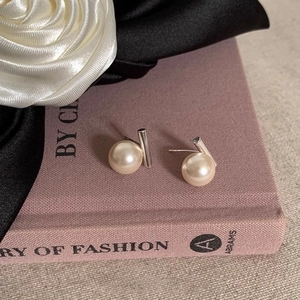 Detail shot of minimalist pearl earrings on a purple book featuring silver metal posts