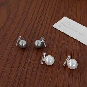 Macro shot of minimalist gray and white pearl stud earrings with silver metal cylinders