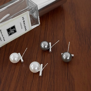 Close-up of minimalist pearl studs set in silver on dark wood, white and grey colors