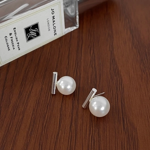 Detail view of minimalist pearl earrings with silver metal bar on a wooden surface